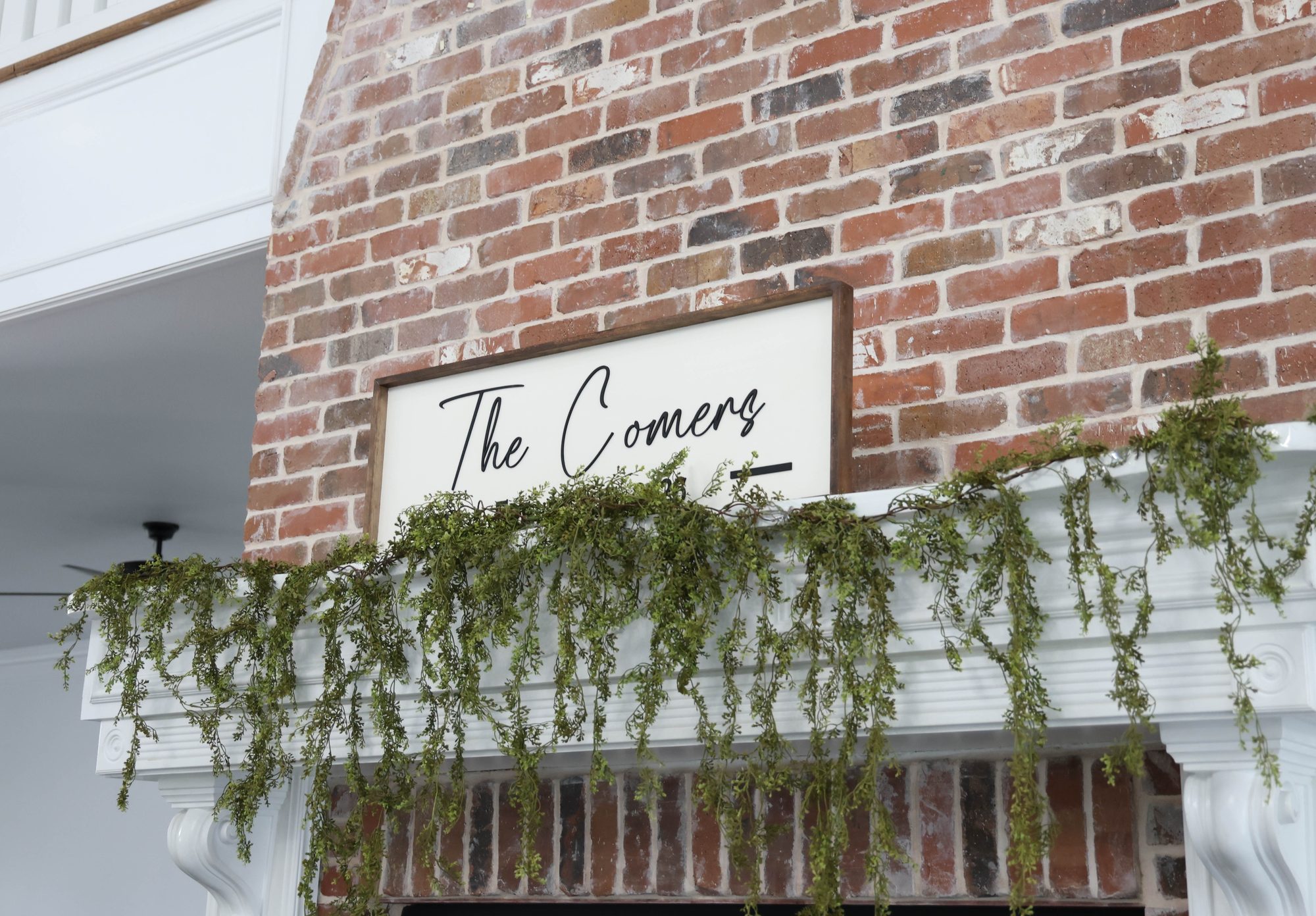 Brick fireplace mantel with a welcome sign and hanging greenery