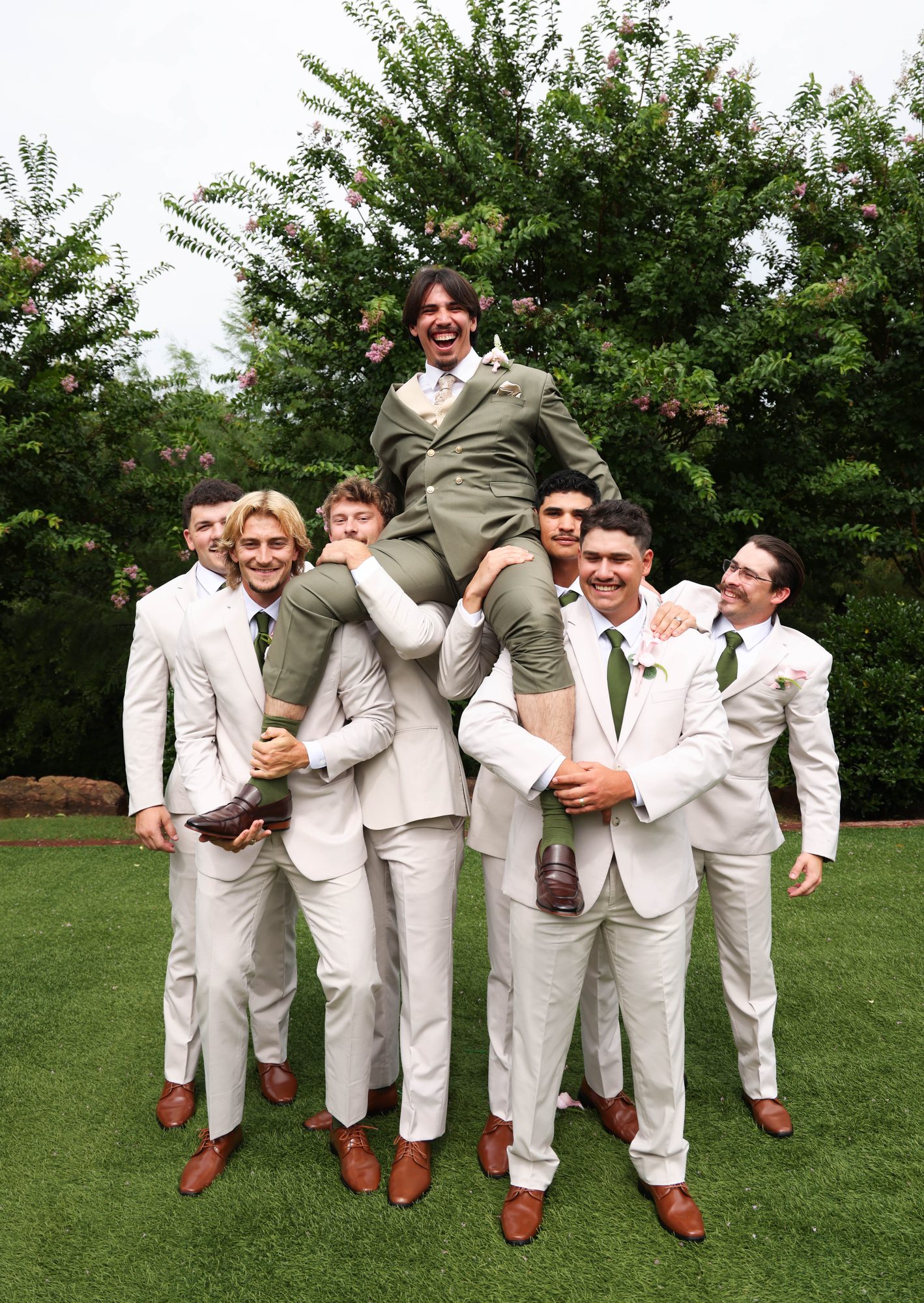 Groomsmen lifting the groom on the lawn